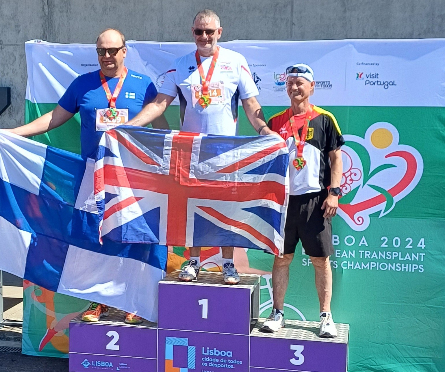 Rob Hodgkiss standing on the first spot of the podium holding the Union Jack